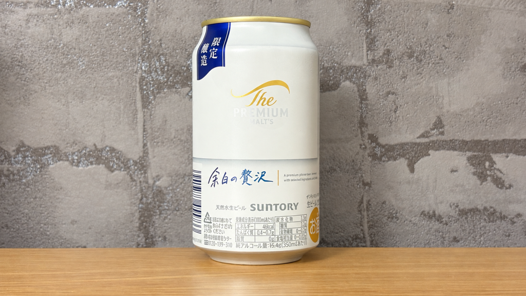 グレーの柄入り壁紙と木の天板を背景に置いたプレモル余白の贅沢の缶