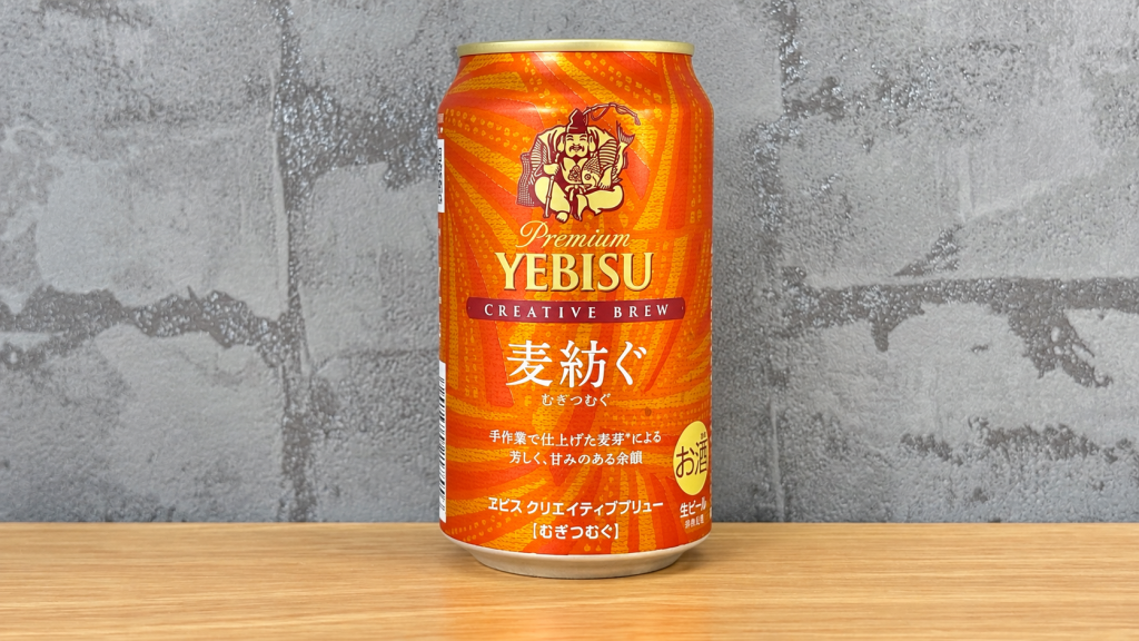 グレーの壁紙を背景に木の天板に置いたヱビス 麦紡ぐの缶