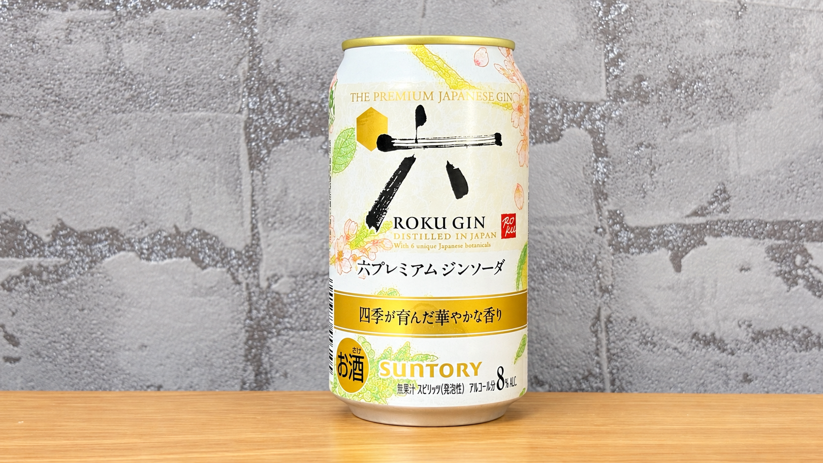 グレーの壁紙と木の天板を背景に置いた六プレミアムジンソーダ缶8％
